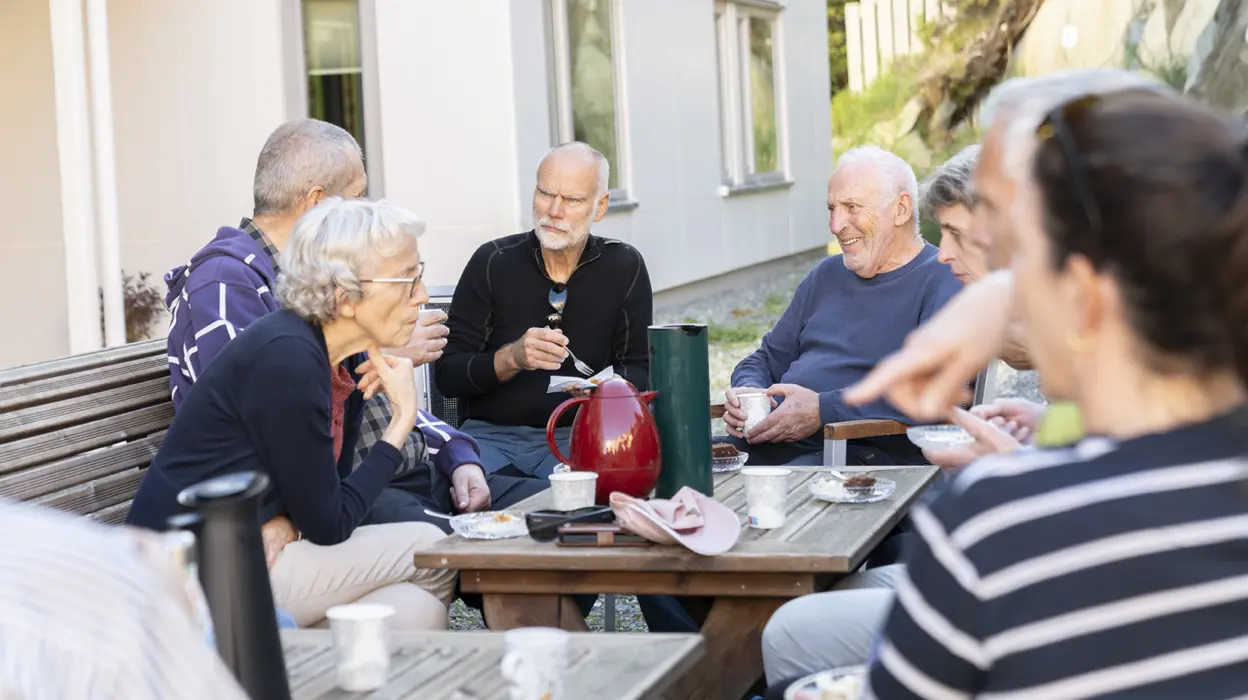 Folk i nabolaget koser seg og drikker kaffe i felles hage