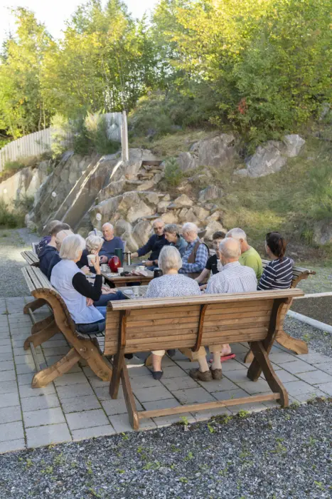Folk fra samme boligblokk koser seg og drikker kaffe i felles hage, nybygget trapp i bakgrunn.